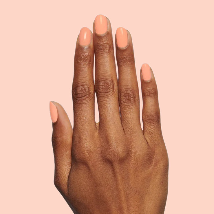 Hand with nails polished in warm coral shade Wild & Free for a vibrant at-home manicure or quick dry polish look
