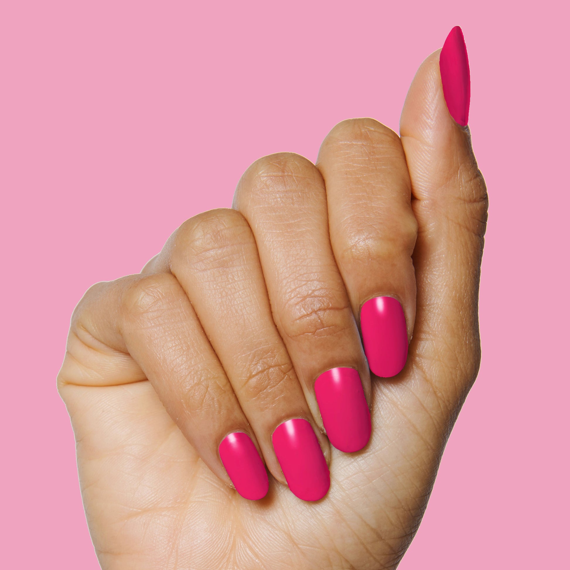 Hand with smooth, bright hot pink nails painted with XOXO long-lasting polish on a solid pink background
