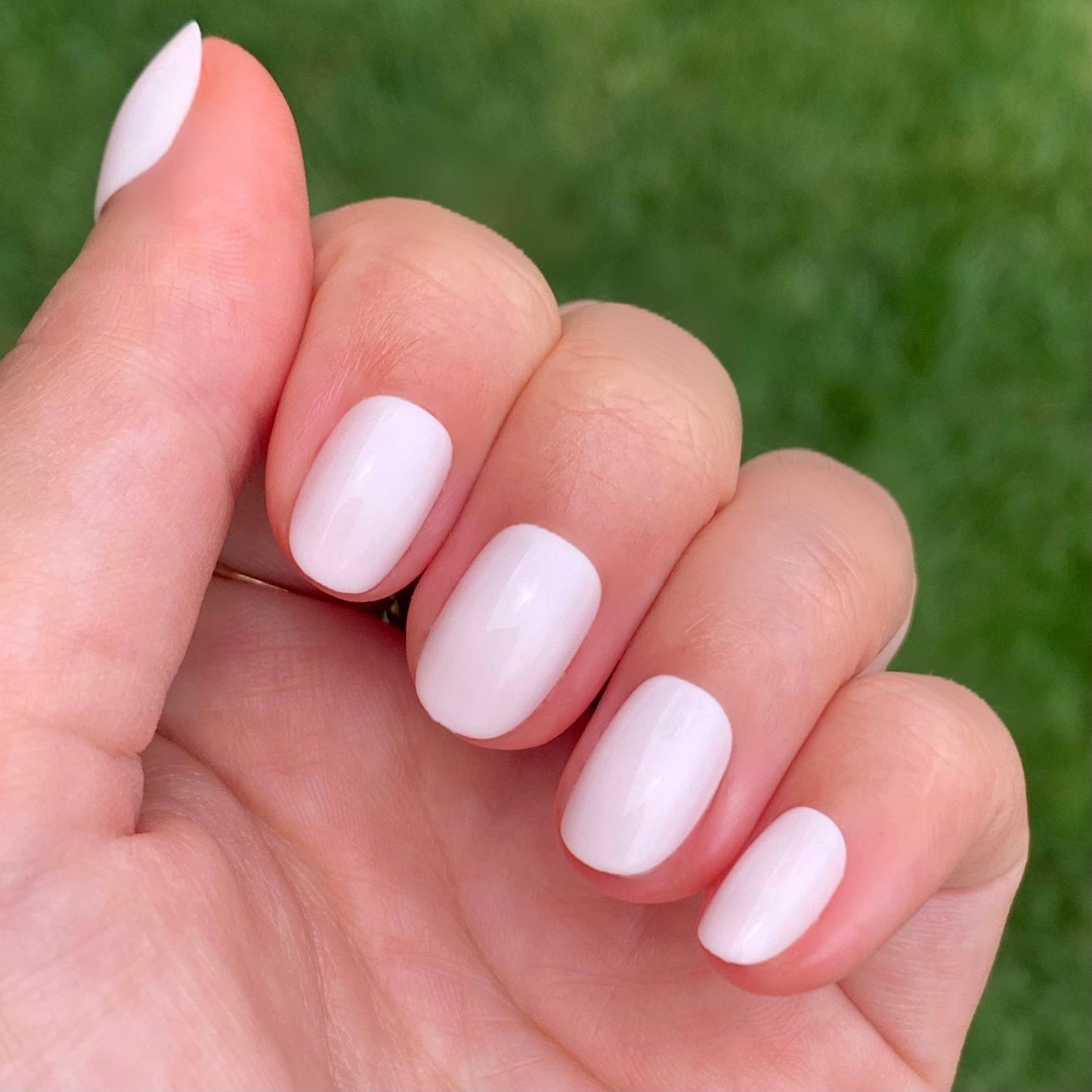 Hand with soft sheer pink nails in an extra short round shape from CCT | Round | Extra Short press-on set