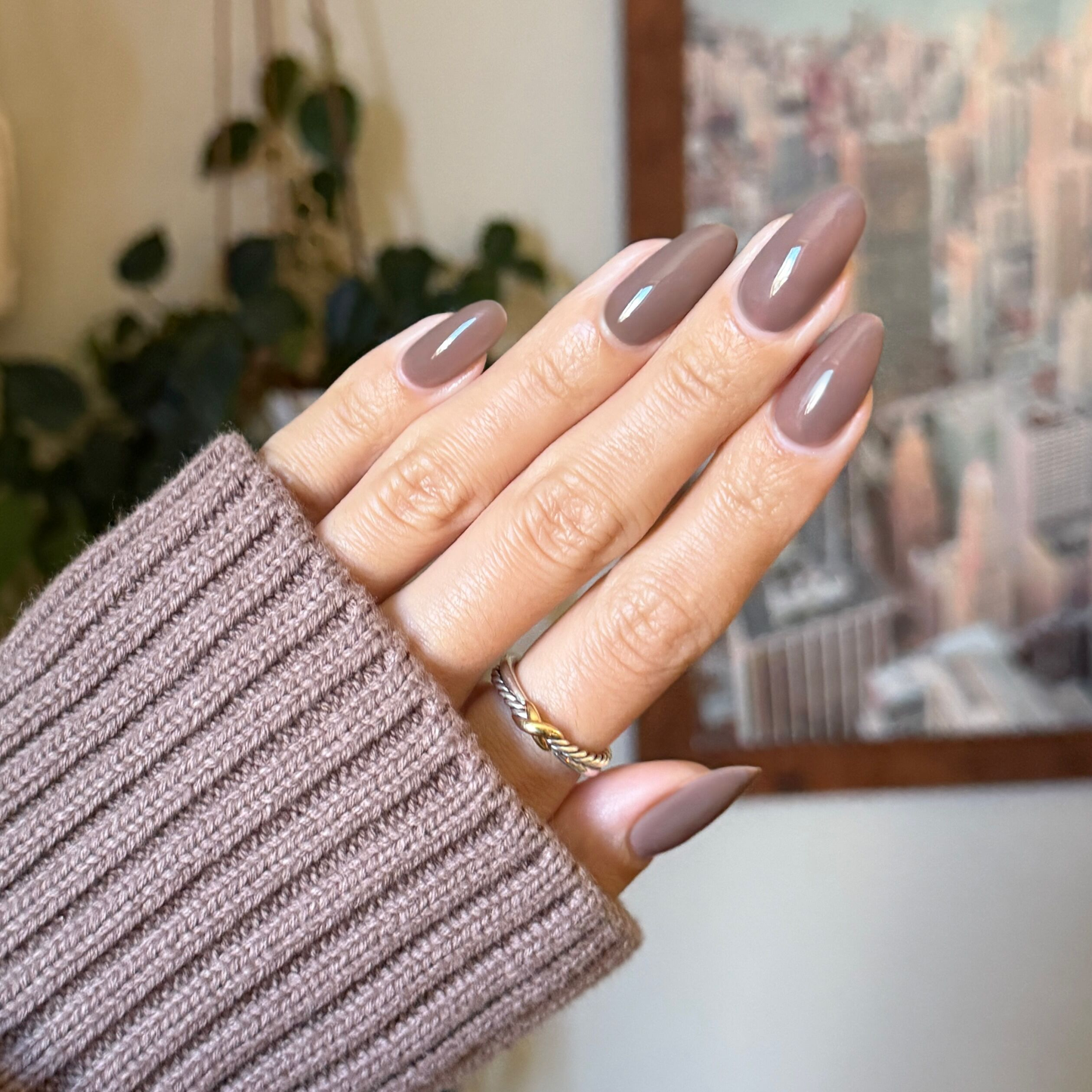 Hand with glossy Fawn - Gel polish in soft minky brown neutral shade, manicured nails with gold ring and cozy sweater sleeve