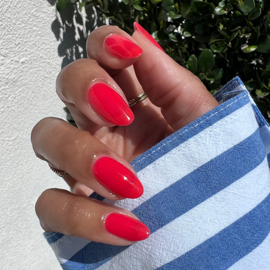 Hand with almond-shaped nails painted in glossy Fragola sheer strawberry pink gel polish showing smooth mani outdoors