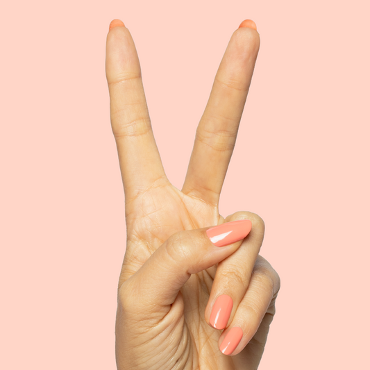 Hand making peace sign with nails painted in bright orangey coral Frolic quick dry gel polish on soft pink background