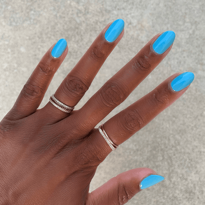 Hand with nails painted in vivid Megababe Blue gel polish showcasing a bright, confident manicure at home