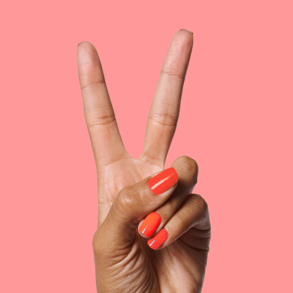 Hand showing a glossy Lava manicure in fiery orange red against a solid soft pink background