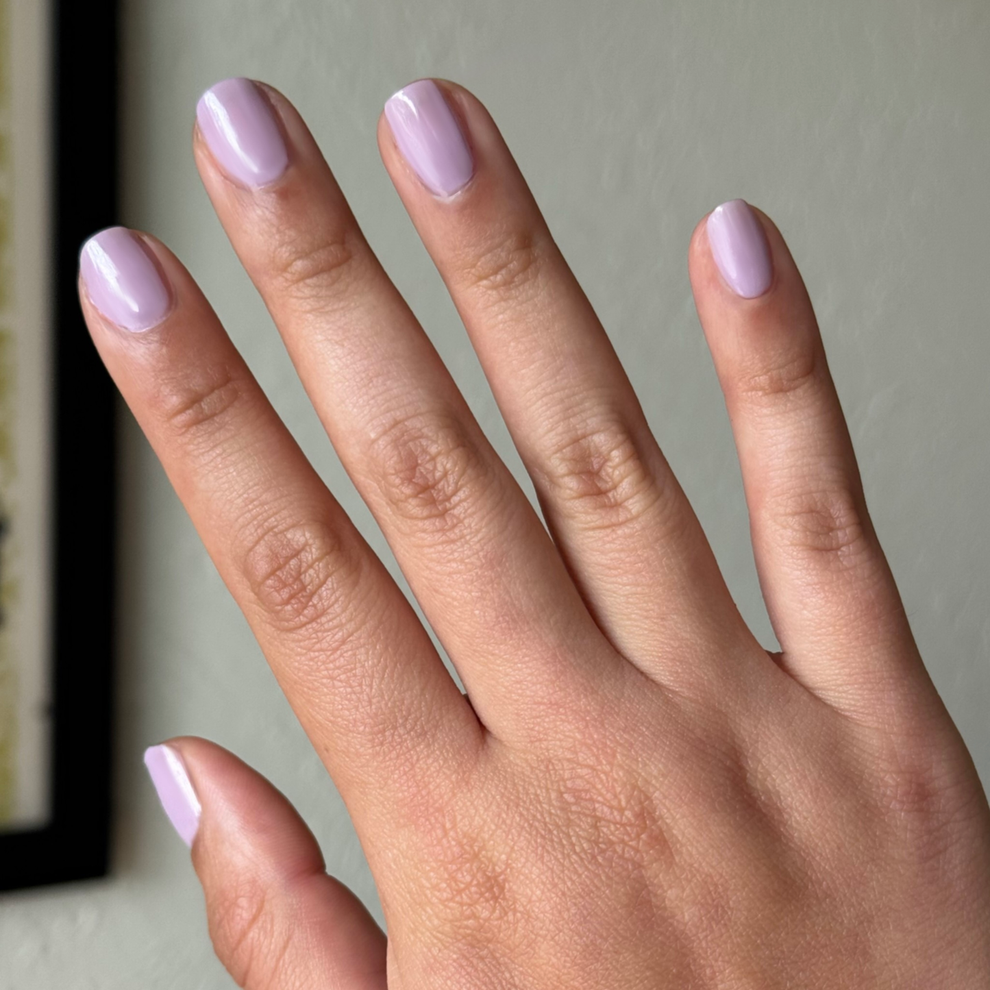 Hand with natural-shaped nails painted in Dreamy sheer milky pastel lavender gel polish for a soft manicure look
