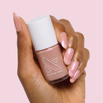 Hand with almond-shaped nails painted in iridescent Sandy Scallop gel polish holding Olive and June nail polish bottle